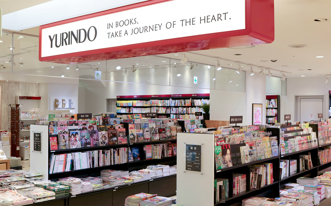 通路沿い天井に赤いフレームで「YURINDO」の看板、雑誌の並ぶ書棚