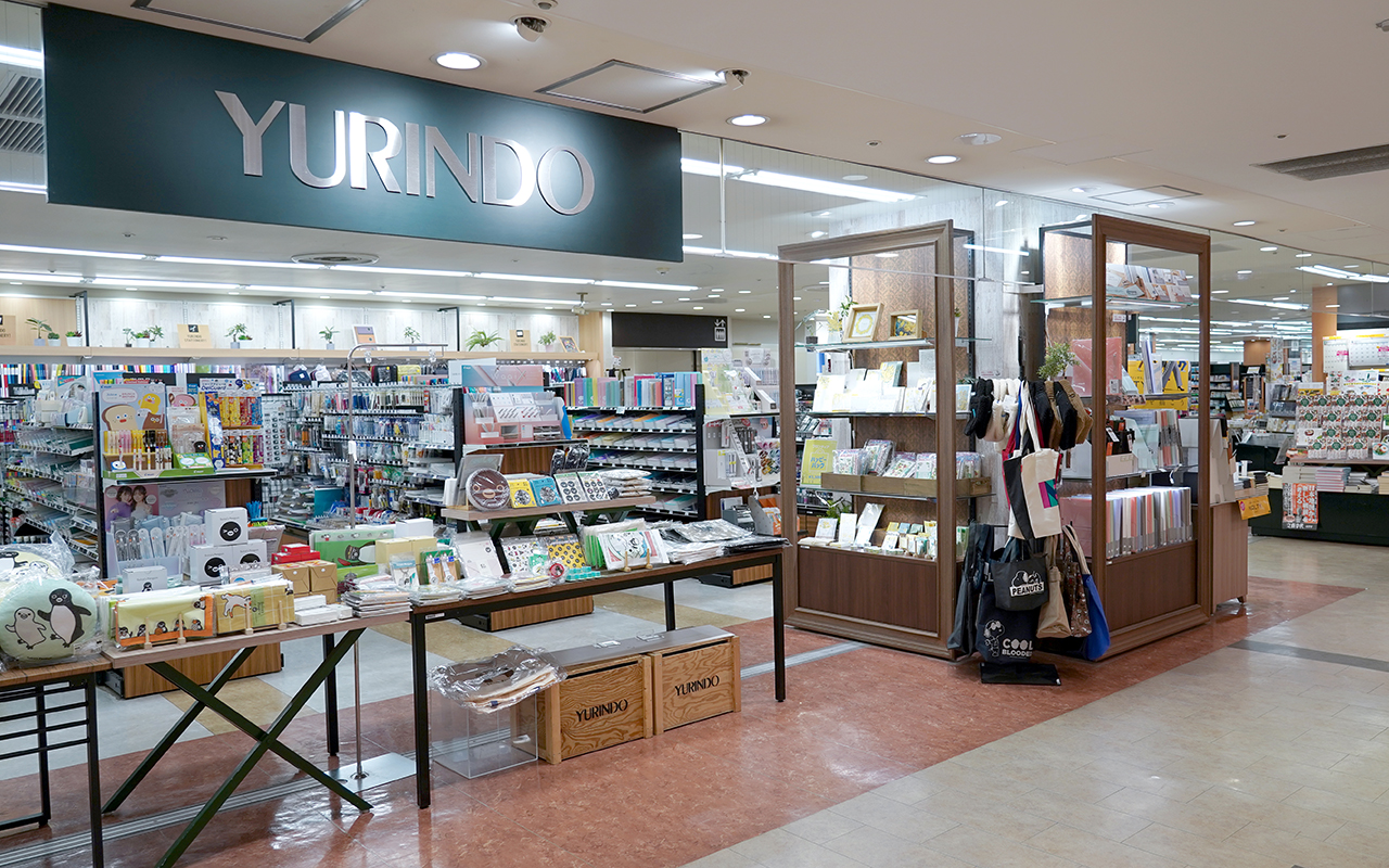 アトレの通路から見た文房具売場、天井に焦げ茶色の「YURINDO」看板が設置され、雑貨のフェアコーナー、奥に文房具の並んだ棚